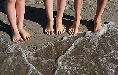 Die nackten Füße einer Familie im Sand und im Wasser 